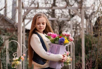 Cute smiling little girl with bouquet of spring flowers in hands outdoor.