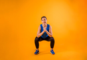 Fototapeta na wymiar a woman in a sports uniform performs squat exercises on an orange isolated background