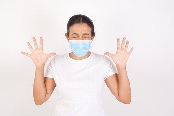 Emotive Young arab woman wearing medical mask standing  laughs loudly, hears funny joke or story, raises palms with satisfaction, being overjoyed, amused by friend. People and emotions concept.