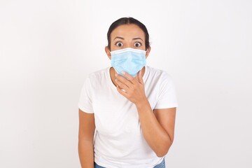 Nervous puzzled Young arab woman wearing medical mask standing over isolated white background, opens mouth from surprise, reacts on sudden news. People and facial expressions.