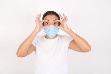 Young arab woman wearing medical mask standing over isolated white background keeping eyes opened to find a success opportunity.