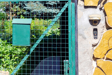 the intercom hangs on a stone wall lined with wood. Next to the green door to the territory of a private house and a mailbox with space for text. Exterior Intercom outside residential building.