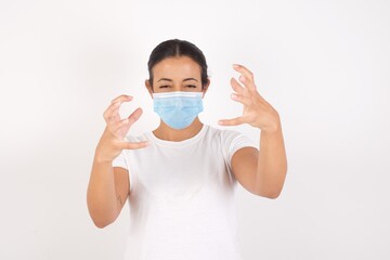 Young arab woman wearing medical mask standing over isolated white background Shouting frustrated with rage, hands trying to strangle, yelling mad.