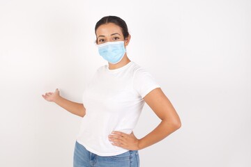 Young arab woman wearing medical mask standing over isolated white background feeling happy and cheerful, smiling and welcoming you, inviting you in with a friendly gesture