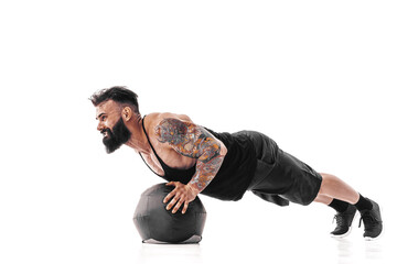 Muscular tattooed bearded male exercising fitness weights Medicine Ball push ups exercises in...