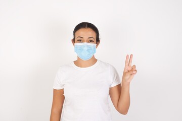 Young arab woman wearing medical mask standing over isolated white background showing and pointing up with fingers number two while smiling confident and happy.