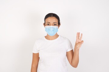 Young arab woman wearing medical mask standing over isolated white background showing and pointing up with fingers number three while smiling confident and happy.