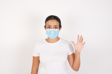 Young arab woman wearing medical mask standing over isolated white background showing and pointing up with fingers number five while smiling confident and happy.