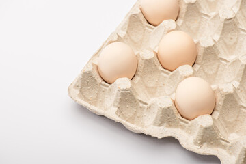 close up view of fresh chicken eggs in cardboard egg tray on white background