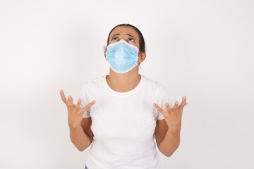 Young arab woman wearing medical mask standing over isolated white background crazy and mad shouting and yelling with aggressive expression and arms raised. Frustration concept.