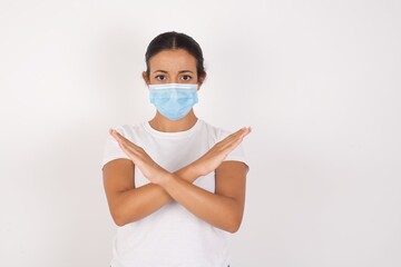 Young arab woman wearing medical mask standing over isolated white background Rejection expression crossing arms doing negative sign, angry face