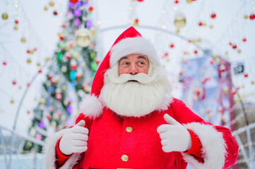 Portrait of an elderly man dressed as santa claus on the background of a christmas tree outdoors.