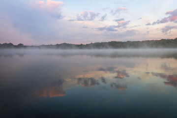 Fog lifts off the lake with dramatic cloudscape at sunrise creating a peaceful relaxing scene with copy space