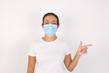 Young arab woman wearing medical mask standing over isolated white background pointing up with fingers number eight in Chinese sign language BÄ.