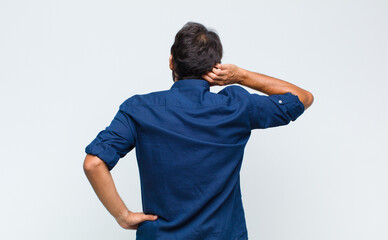 young latin handsome man thinking or doubting, scratching head, feeling puzzled and confused, back...