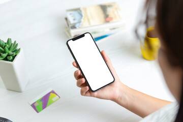 Phone mockup in woman hand. Work desk in background with credit card, plant, books, and coffee mug