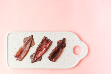 Fresh ancooked squids on white plate on pink background. Top view. Space for text.