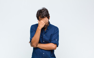 young latin handsome man looking stressed, ashamed or upset, with a headache, covering face with...