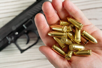 Yellow golden coloured bullets held in hand, blurred wooden desk with black gun under