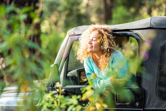 People enjoying freedom and the good of a travel lifestyle - cheerful happy woman outside the car window snjoy the sun - alternative road trip vacation in the forest with all terrain vehicle