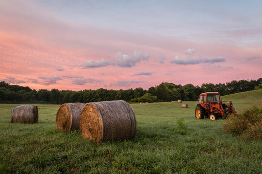 Freshly rolled hay bales rest on rolling hill with dramatic cloudscape at sunrise creating a rustic rural scene in Sussex County, NJ