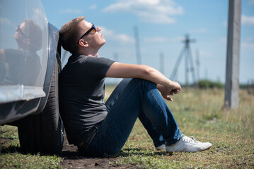 A driver is sitting on the ground near broken car.