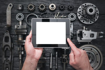 Car service worker is holding a blank screen digital tablet above spare parts background. Car spare parts order online concept.