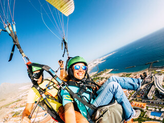 Cheerful happy woman to paraglyde experience with pilot - couple having fun in the air paraglyding...