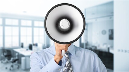 Young businessman talking on the megaphone on office background