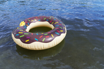 An inflatable circle in the form of a bitten doughnut floats on the water in the river. In the clear water bottom of the river and reflection of doughnut can be seen. Focus on the far side of doughnut