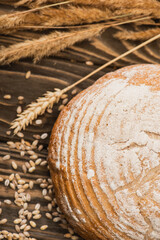 selective focus of fresh baked bread loaf with spikelets on wooden surface