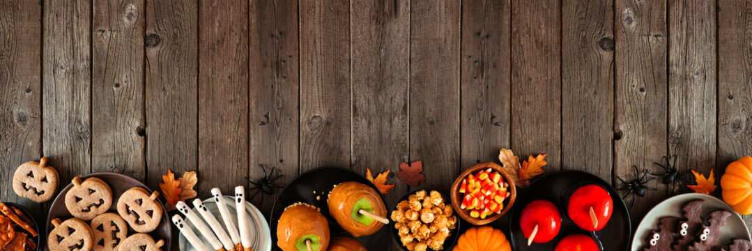 Rustic Halloween treat bottom border over a dark wood banner background with copy space. Above view. Variety of candied apples, cookies, candy and sweets. - Powered by Adobe