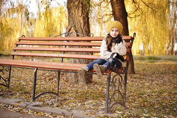 Cheerful preschooler little girl in coat and yellow hat with autumn leaves in the park. Child portrait. Cute kid girl 4-5 year old posing outdoors, has happy face. Walking in park. Childhood.