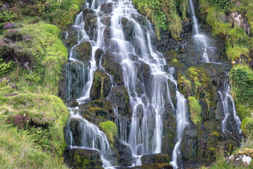 View of Bride Veil waterall on the Isle of Skye, Scotland. Beautiful collection of many smaller falls flowing in different directions. Fern and blooming heather around