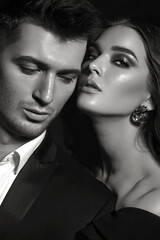 Beautiful young stylish couple, man and woman, in black evening dresses in each other's arms posing in the studio on a black background.