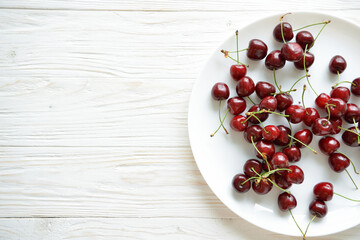 View from above of ripe red cherry in white plate on wooden background with space for text. Top view concept. Layout food background