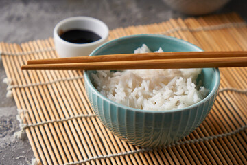 Rice in a porcelain bowl, with Japanese chopsticks, soy sauce, served on a gray stone table