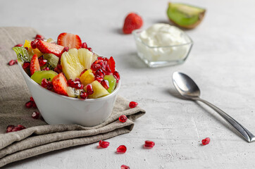 fruit salad with yogurt and pomegranate in a white bowl