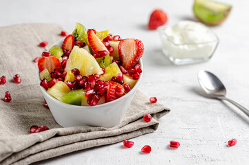 fruit salad with yogurt and pomegranate in a white bowl