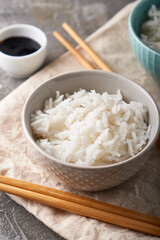 Rice in a porcelain bowl, with Japanese chopsticks, soy sauce, served on a gray stone table