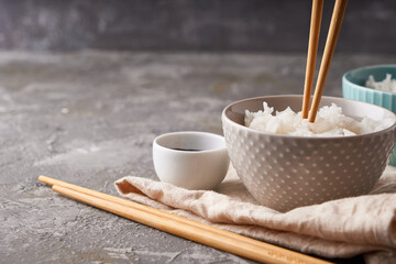 Rice chopsticks, over a bowl of white rice, soy sauce on a dark gray background