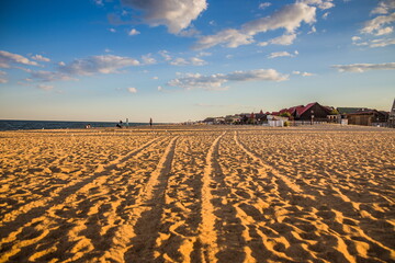 Beautiful evening beach. Shadows fall on the sand. Sea sand in the light of the setting sun. Tire tracks in the sand