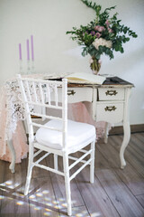 Front view of antique toilet table and white chiavari chair in the light room with decorative elements, place for writing, romantic space, bouquet made of greenery and violet candles, peopleless