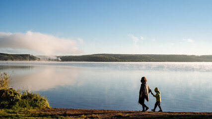 mother leads her son by the hand along the lake shore, family walk along the river Bank, meet the...