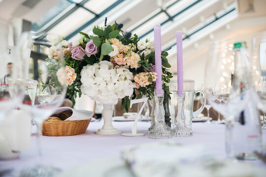 White table serving with violet candles and floral composition made of white hydrangea and violet rose at the restaurant, wedding preparing, wedding celebration, elegant table party decoration