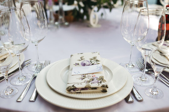 White plates with serviette and guest card, empty glasses, cutlery, decorated wedding table, minamalism decoration of celebration, elegant gala dishes, table serving, restaurant serving
