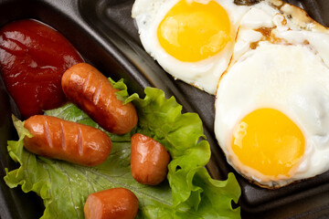 Fried eggs with sausages and croutons on a dark background. Scrambled eggs in a disposable plate close-up.
