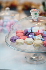 Fototapeta na wymiar Delicious colorful macarons in the glass tray, front view of sweet patisserie, wedding candy bar, sweet buffet on the birthday party celebration, restaurant sweet catering