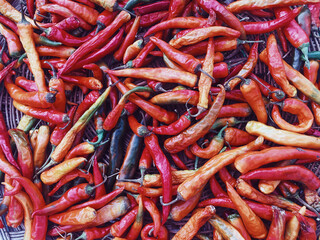 Dried peppers in different colors lying in a wicker basket, flat top view,