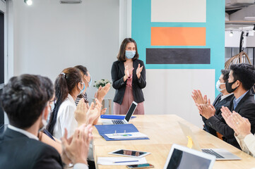 Multi ethnic colleagues celebrating with applauding the female executive while meeting in new normal office. Business team wearing face mask